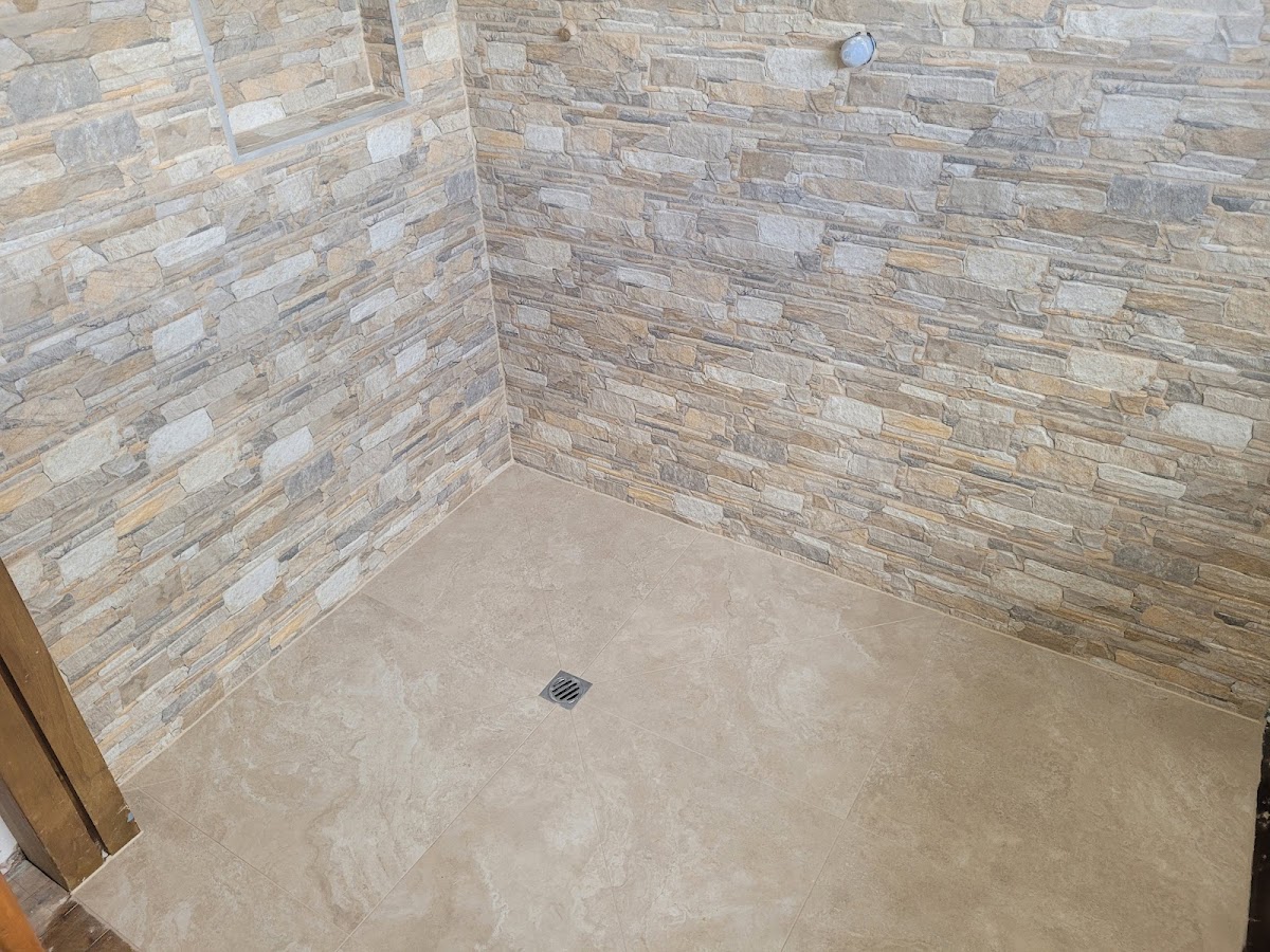 Stacked schist stone feature wall with large-format floor tiling and a tiled floor drain by Summit Tiling